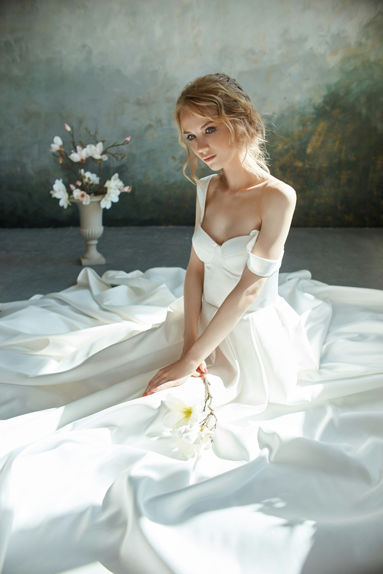 Girl in a chic long dress sitting on the floor. White wedding dress on the bride's body